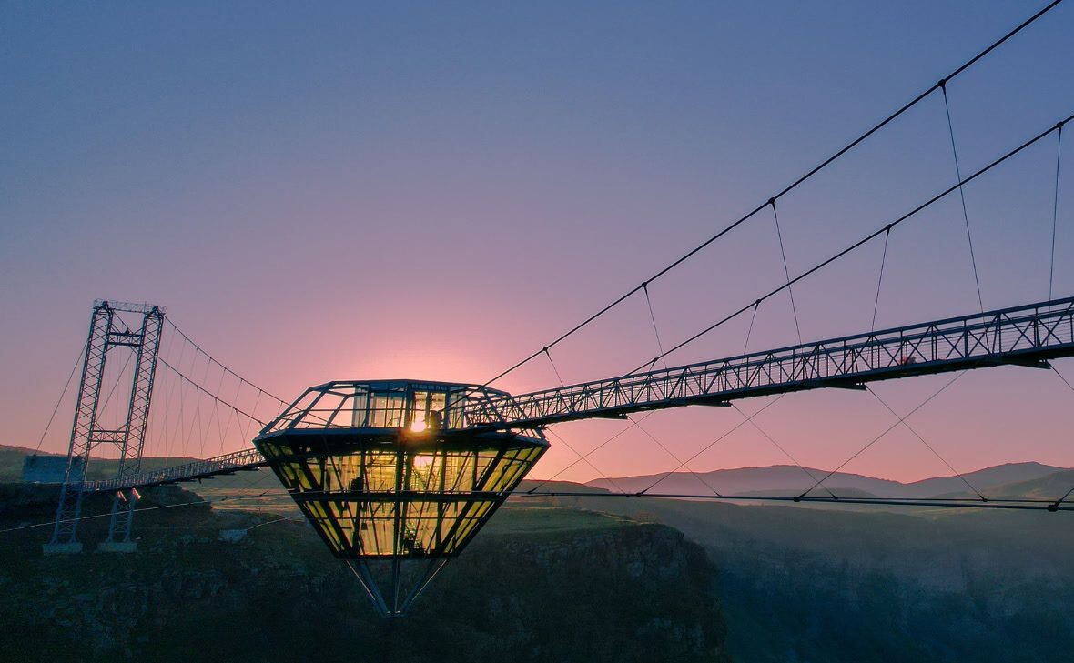 Suspension bridge with a glass structure at sunrise over a canyon.