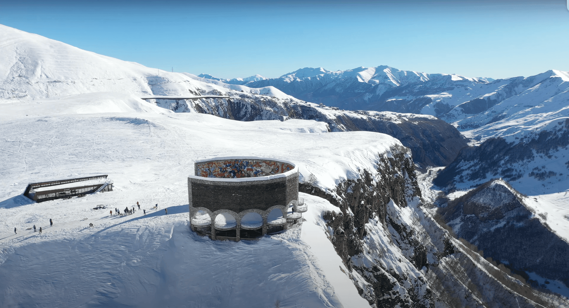 Circular stone monument with colorful mural on a snowy mountain landscape.