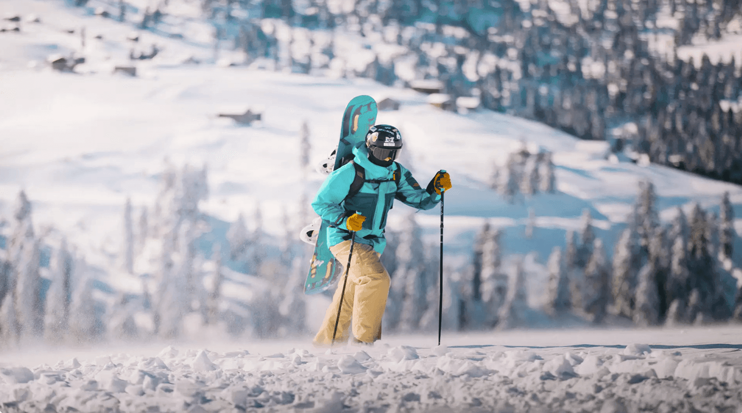 Person wearing ski gear with snowboard on back walks through snowy landscape with poles.