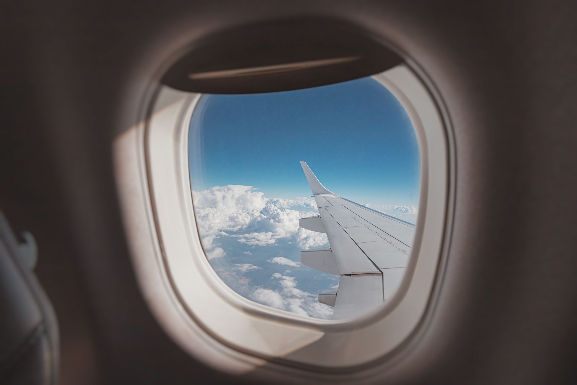 view from the porthole captures a stunning horizon, showcasing the airplane wing against a backdrop of blue skies and fluffy clouds